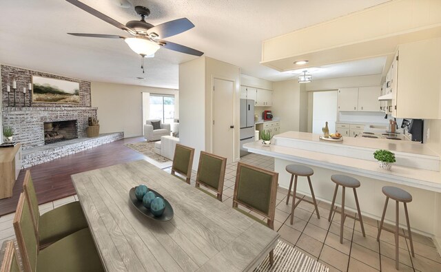 kitchen with white cabinetry, a kitchen breakfast bar, a brick fireplace, kitchen peninsula, and light wood-type flooring