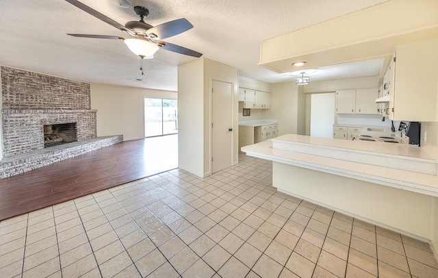 kitchen with a textured ceiling, kitchen peninsula, ceiling fan, a fireplace, and white cabinets