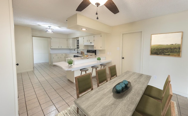 kitchen with a textured ceiling, white cabinets, a kitchen bar, and kitchen peninsula