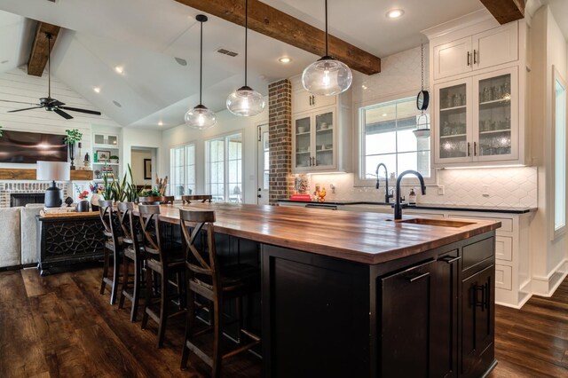 kitchen featuring dark hardwood / wood-style flooring, butcher block counters, a kitchen island with sink, and white cabinets