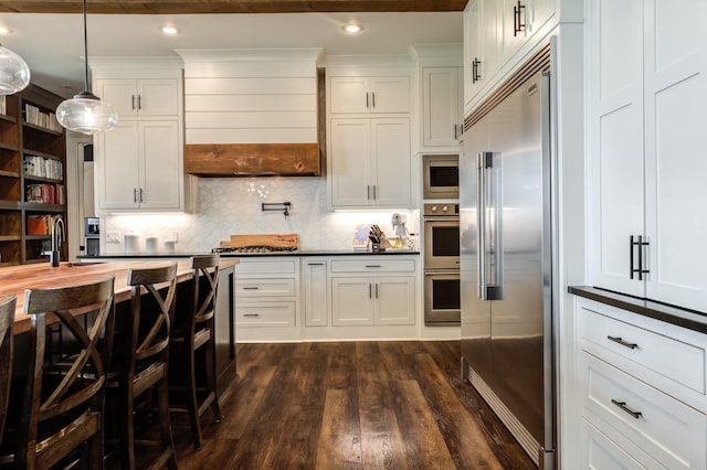 kitchen with decorative light fixtures, white cabinetry, custom exhaust hood, built in appliances, and dark wood-type flooring