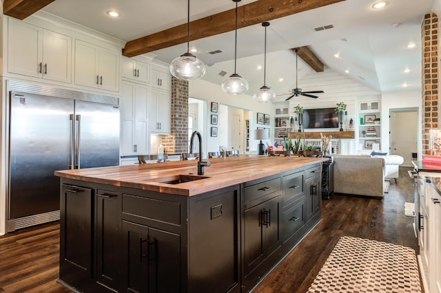 kitchen featuring white cabinetry, stainless steel built in fridge, a kitchen island with sink, and butcher block countertops