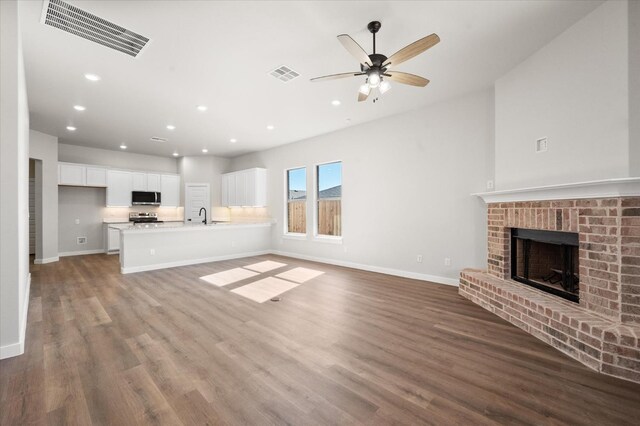 unfurnished living room with a brick fireplace, sink, hardwood / wood-style floors, and ceiling fan