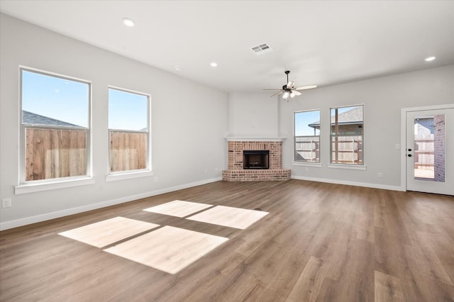 unfurnished living room with a brick fireplace, hardwood / wood-style floors, a healthy amount of sunlight, and ceiling fan