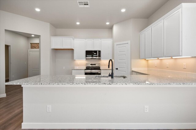 kitchen featuring appliances with stainless steel finishes, sink, white cabinets, light stone counters, and dark wood-type flooring