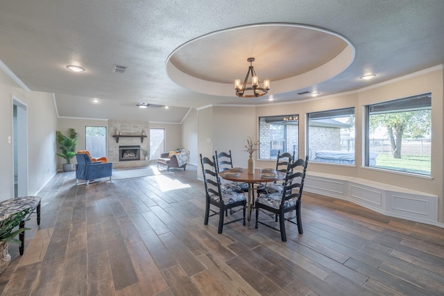 dining space with a raised ceiling, dark wood-type flooring, a fireplace, and a textured ceiling