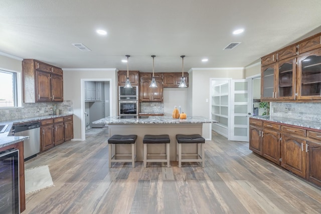 kitchen with wine cooler, hanging light fixtures, a kitchen island, stainless steel appliances, and light stone countertops