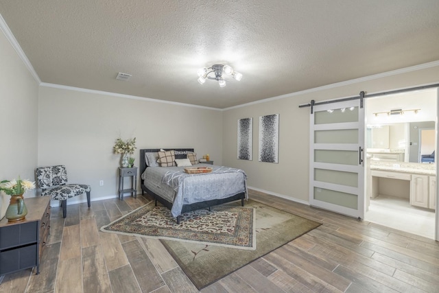 bedroom with crown molding, ensuite bath, wood-type flooring, a textured ceiling, and a barn door