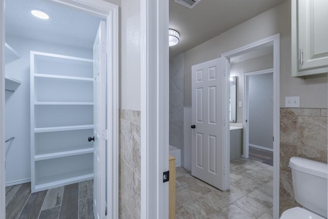 bathroom featuring toilet and tile walls