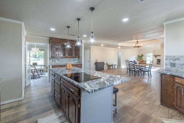 kitchen with hardwood / wood-style flooring, dark brown cabinets, ornamental molding, a kitchen island, and black electric cooktop