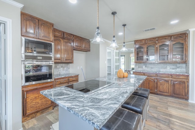 kitchen with light stone countertops, a kitchen island, light hardwood / wood-style flooring, and black appliances