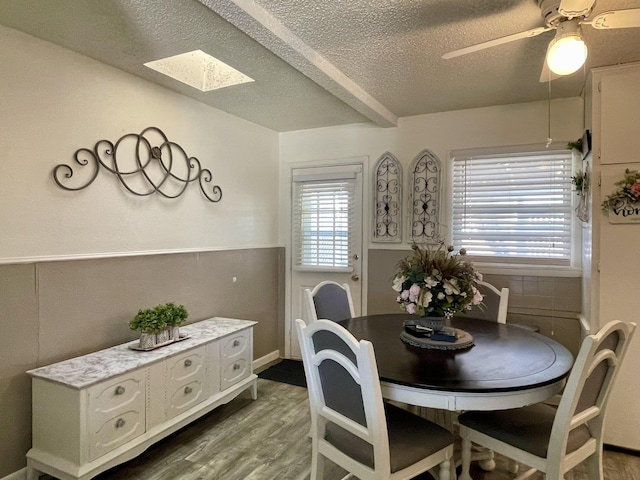 dining space with a ceiling fan, wood finished floors, a textured ceiling, and a skylight