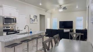 kitchen with ceiling fan, appliances with stainless steel finishes, white cabinetry, light stone countertops, and a kitchen bar