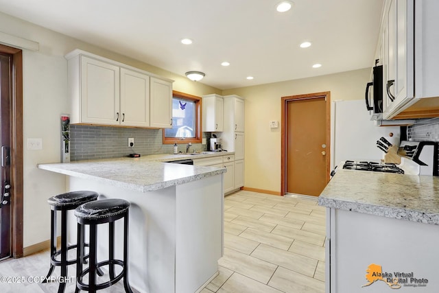 kitchen featuring white cabinets, light countertops, white range with gas stovetop, and black microwave