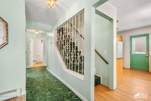 hall with a baseboard radiator, light hardwood / wood-style flooring, and a textured ceiling