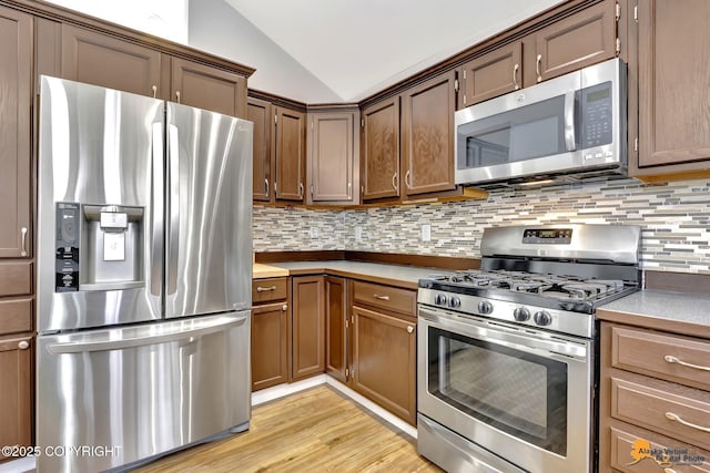 kitchen with light countertops, backsplash, light wood-style flooring, appliances with stainless steel finishes, and vaulted ceiling