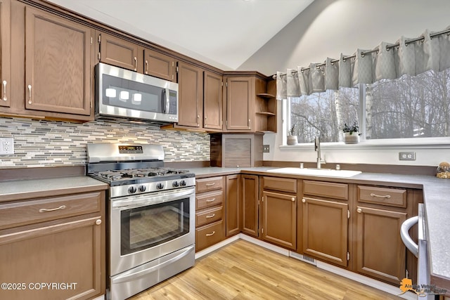 kitchen featuring stainless steel appliances, light countertops, brown cabinetry, vaulted ceiling, and a sink