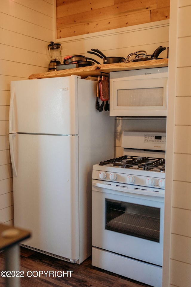 kitchen featuring white appliances, dark wood-type flooring, and wooden walls