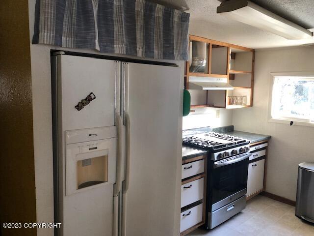 kitchen featuring a textured ceiling, stainless steel range with gas cooktop, and white refrigerator with ice dispenser