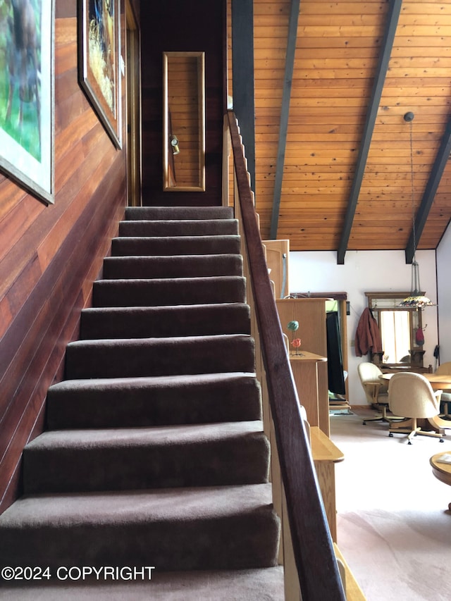 staircase featuring wood walls, wood ceiling, carpet, and beamed ceiling