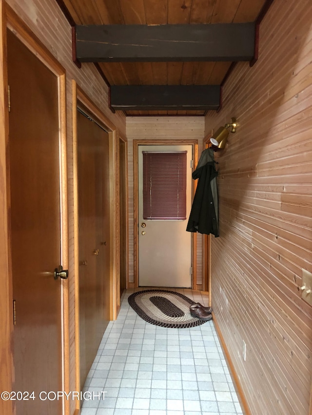 corridor featuring wood walls, tile patterned flooring, beamed ceiling, and wooden ceiling