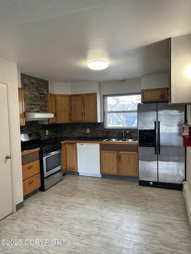 3940 E 9th Ave, Anchorage, AK 99508 - kitchen with a sink, dark countertops, light wood-style floors, under cabinet range hood, and appliances with stainless steel finishes