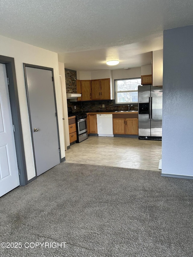 3940 E 9th Ave, Anchorage, AK 99508 - kitchen featuring brown cabinets, stainless steel appliances, dark countertops, light carpet, and tasteful backsplash