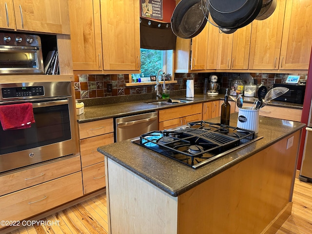 kitchen featuring appliances with stainless steel finishes, sink, light wood-type flooring, a center island, and tasteful backsplash