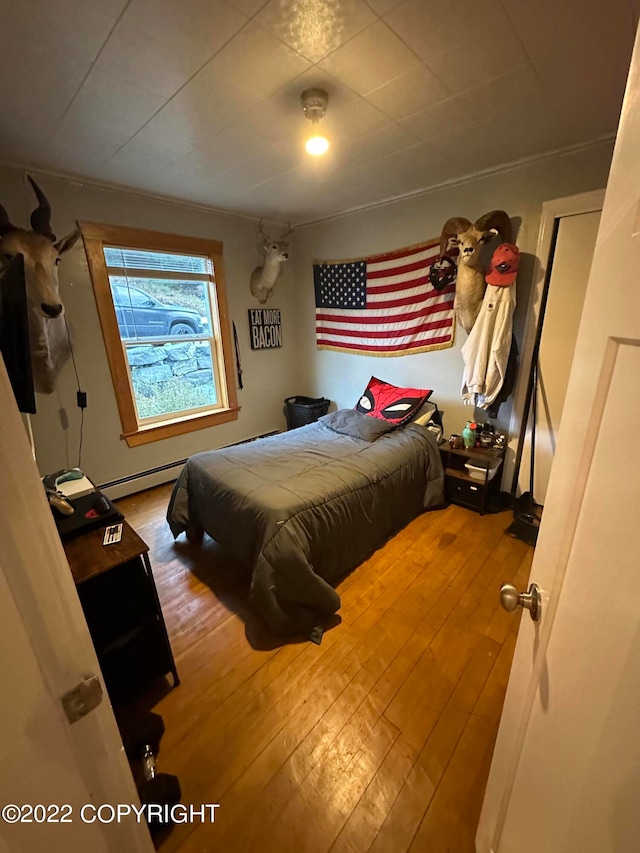 bedroom featuring a baseboard heating unit, ornamental molding, and light hardwood / wood-style floors