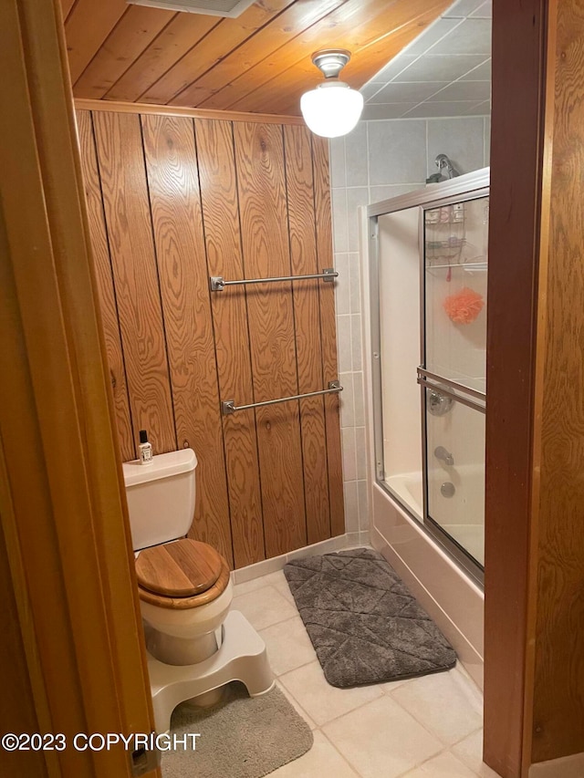 bathroom with toilet, wood walls, wooden ceiling, tile flooring, and bath / shower combo with glass door