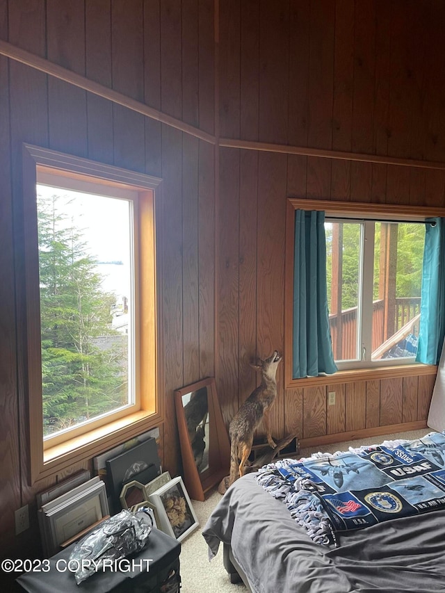 bedroom with carpet floors, wood walls, and multiple windows