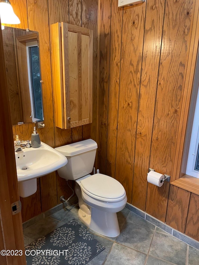 bathroom with toilet, wood walls, tile floors, and sink