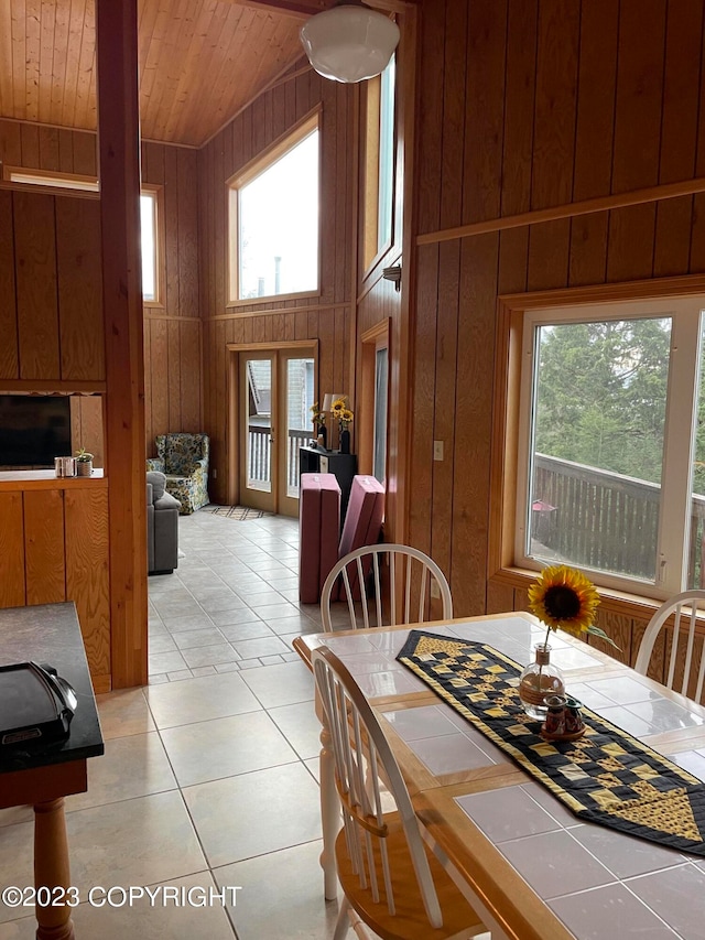 tiled dining space with high vaulted ceiling, wood ceiling, and wood walls