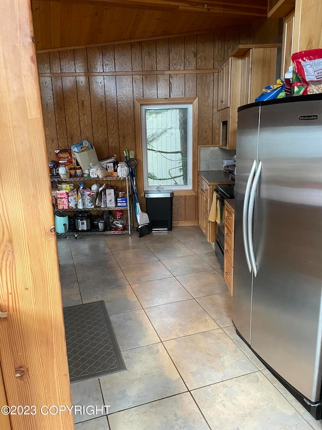 kitchen with stainless steel fridge, wooden walls, light tile flooring, and electric range