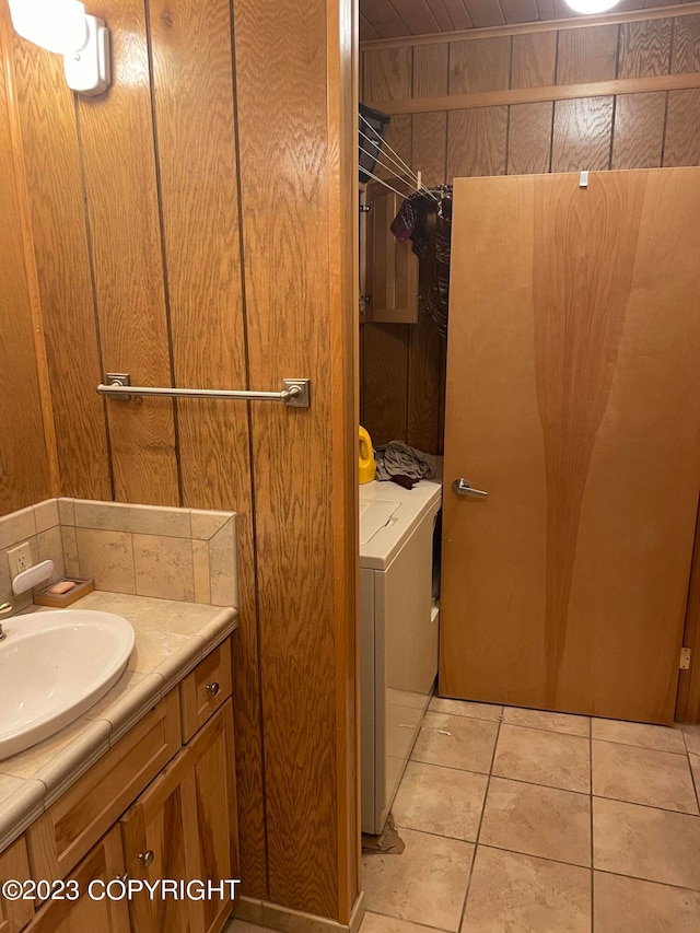 bathroom with wooden walls, tile flooring, washer and clothes dryer, and vanity