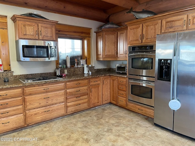 kitchen featuring beam ceiling, appliances with stainless steel finishes, light tile floors, and dark stone countertops