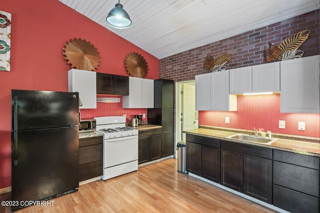 kitchen featuring white gas range, decorative light fixtures, brick wall, black refrigerator, and light hardwood / wood-style flooring