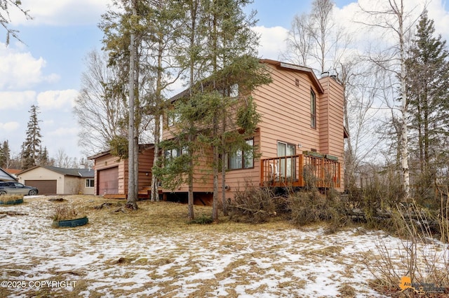 view of snowy exterior with a garage and a chimney