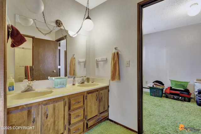 full bath featuring a textured ceiling, double vanity, a sink, and baseboards