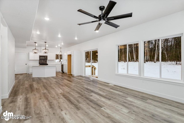 unfurnished living room featuring ceiling fan with notable chandelier and light wood-type flooring