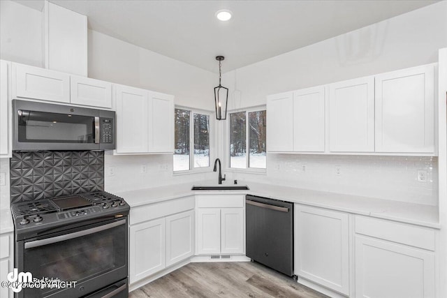 kitchen featuring white cabinets, decorative light fixtures, stainless steel appliances, light wood-type flooring, and sink