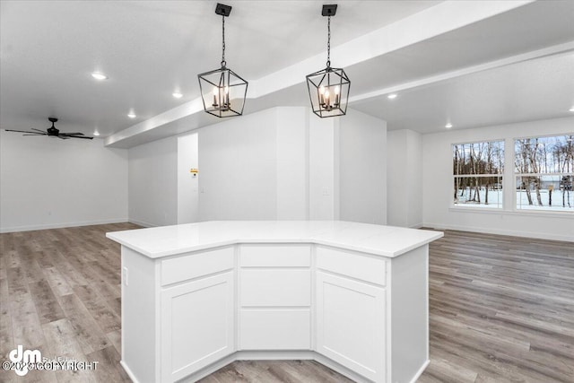 kitchen featuring light hardwood / wood-style floors, hanging light fixtures, white cabinetry, a kitchen island, and ceiling fan with notable chandelier