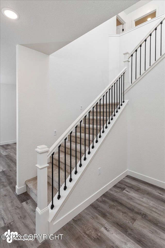 stairway featuring recessed lighting, a textured ceiling, baseboards, and wood finished floors