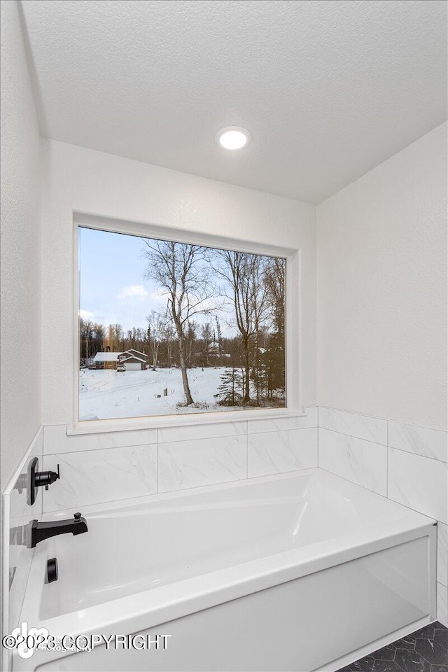 bathroom featuring a bath to relax in, a textured ceiling, and a wealth of natural light