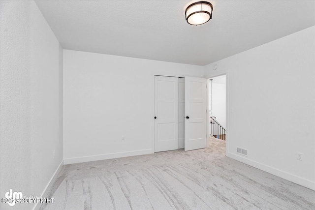 carpeted spare room with baseboards, visible vents, and a textured ceiling