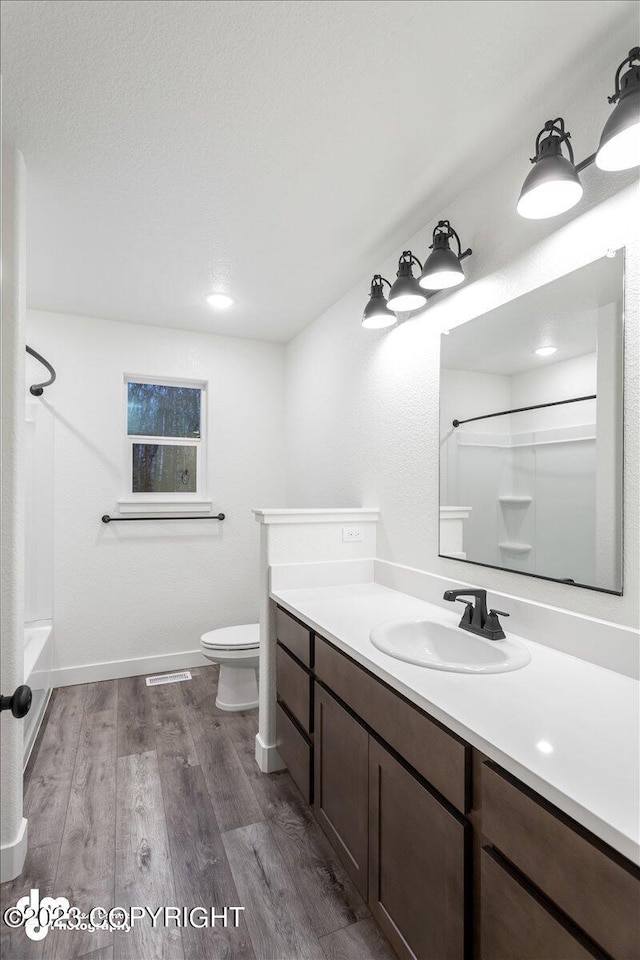 bathroom with vanity, wood finished floors, baseboards,  shower combination, and toilet