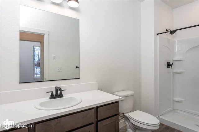 bathroom featuring vanity, toilet, a textured wall, and a stall shower