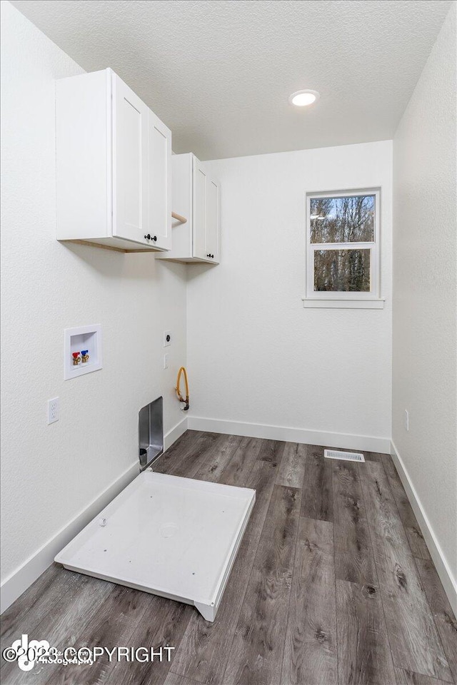 laundry area featuring hookup for a washing machine, baseboards, cabinet space, dark wood-type flooring, and a textured ceiling