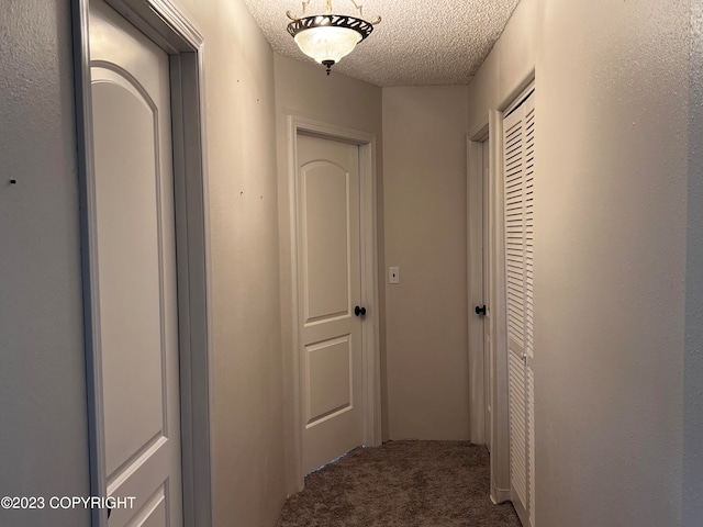 hallway featuring a textured ceiling and dark carpet