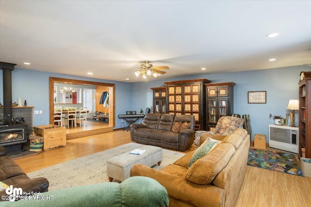 living area with recessed lighting, wood finished floors, a wood stove, and ceiling fan with notable chandelier